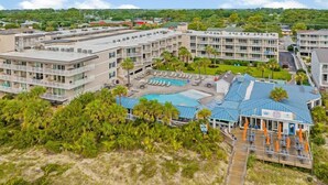 Un complexe hôtelier comprenant plusieurs bâtiments, un espace piscine central et un bar situé en bord de plage.