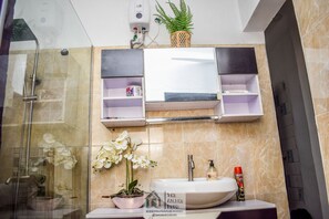A bathroom with a glass shower enclosure, a sink with a white basin, a potted orchid, and a shelf with toiletries. - Beautiful One Bed Apartment in Lekki Phase1 (Lekki)