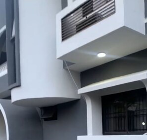 A modern building with a grey facade, a visible air conditioning unit, and a window with a metal grille. - Beautiful One Bed Apartment in Lekki Phase1 (Lekki)