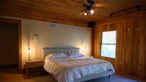 A bedroom with a wooden ceiling, a bed with white bedding, a nightstand with a lamp, and a window with blinds. - Star Ridge | Private Estate | Sleeps 20 | Hot Tub (Wood Township)