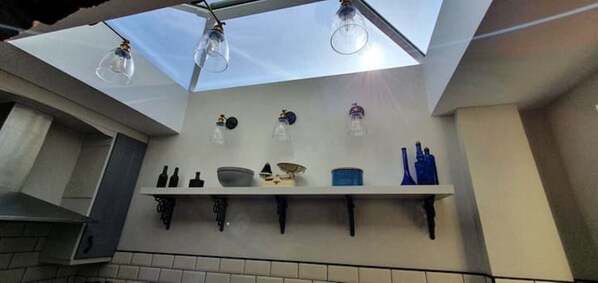 A kitchen with a skylight, white shelves, and various kitchen items.