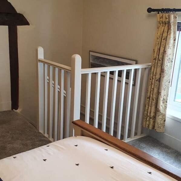 A bedroom with a white bed, a wooden headboard, a white crib, and a window with floral curtains. - Victory Cottage -Ludlow -A Cosy Romantic Escape (ludlow)