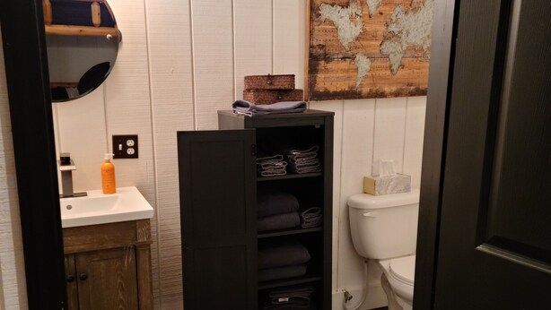 A compact bathroom with a wooden vanity, a black cabinet with shelves, a white toilet, and a world map on the wall.