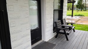 A porch with a bench and a door, a welcome sign, and a grassy yard in the background.
