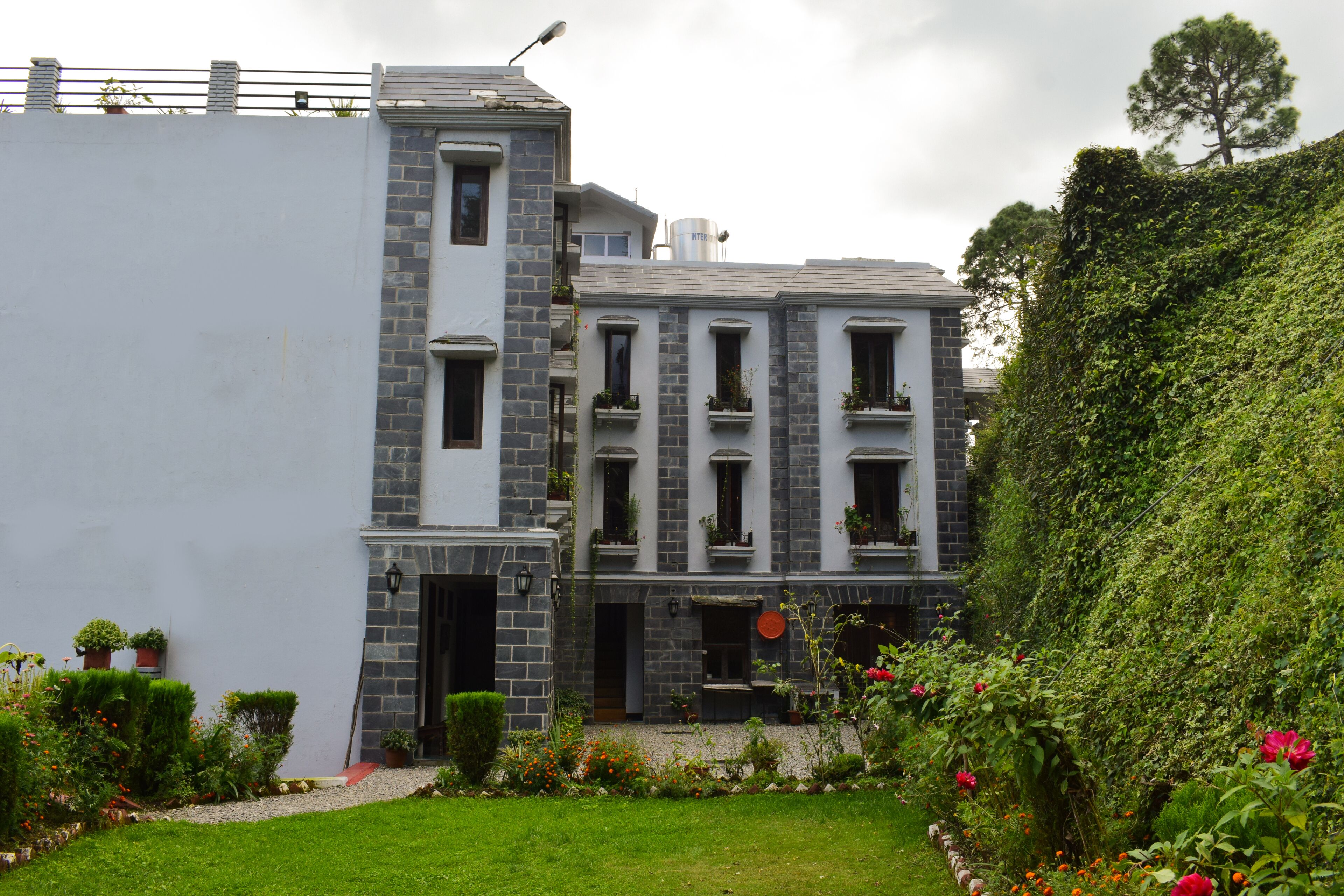 A two-story building with a stone facade, multiple windows, and a small garden with various plants and flowers.