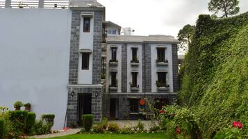 A two-story building with a stone facade, multiple windows, and a small garden with various plants and flowers.