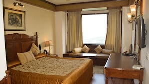 A hotel room with a large bed, a desk, a chair, a sofa, and a window with curtains. - Sun N Snow Inn By Leisure Hotels (Somashwar)