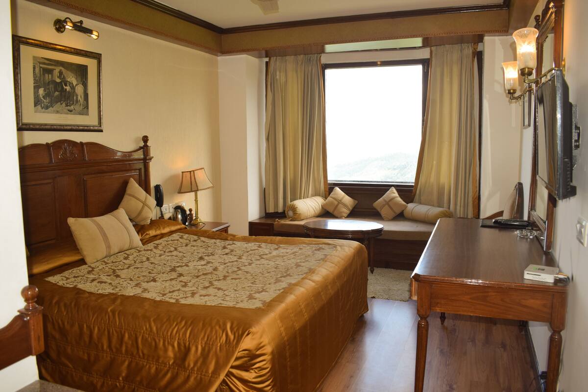 Ein Hotelzimmer mit einem großen Bett, einem Schreibtisch, einem Stuhl, einer Couch und einem fensterbepflanzten Fenster.