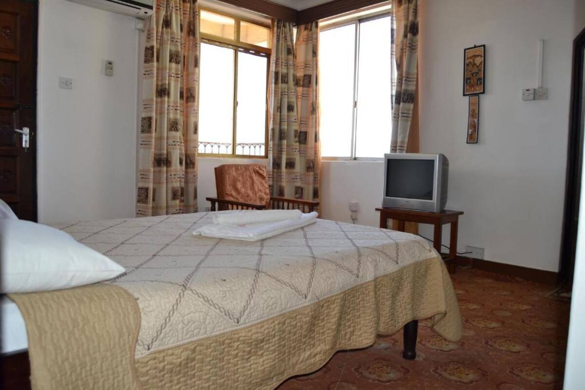 Une chambre à coucher avec un lit, un téléviseur posé sur une table de chevet et une fenêtre avec des rideaux.