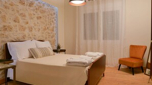 A bedroom with a bed, a chair, a nightstand, a lamp, and a window with curtains.