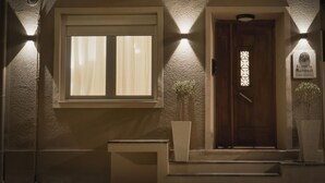 A hotel entrance with a wooden door, a window with blinds, and two wall-mounted lights.