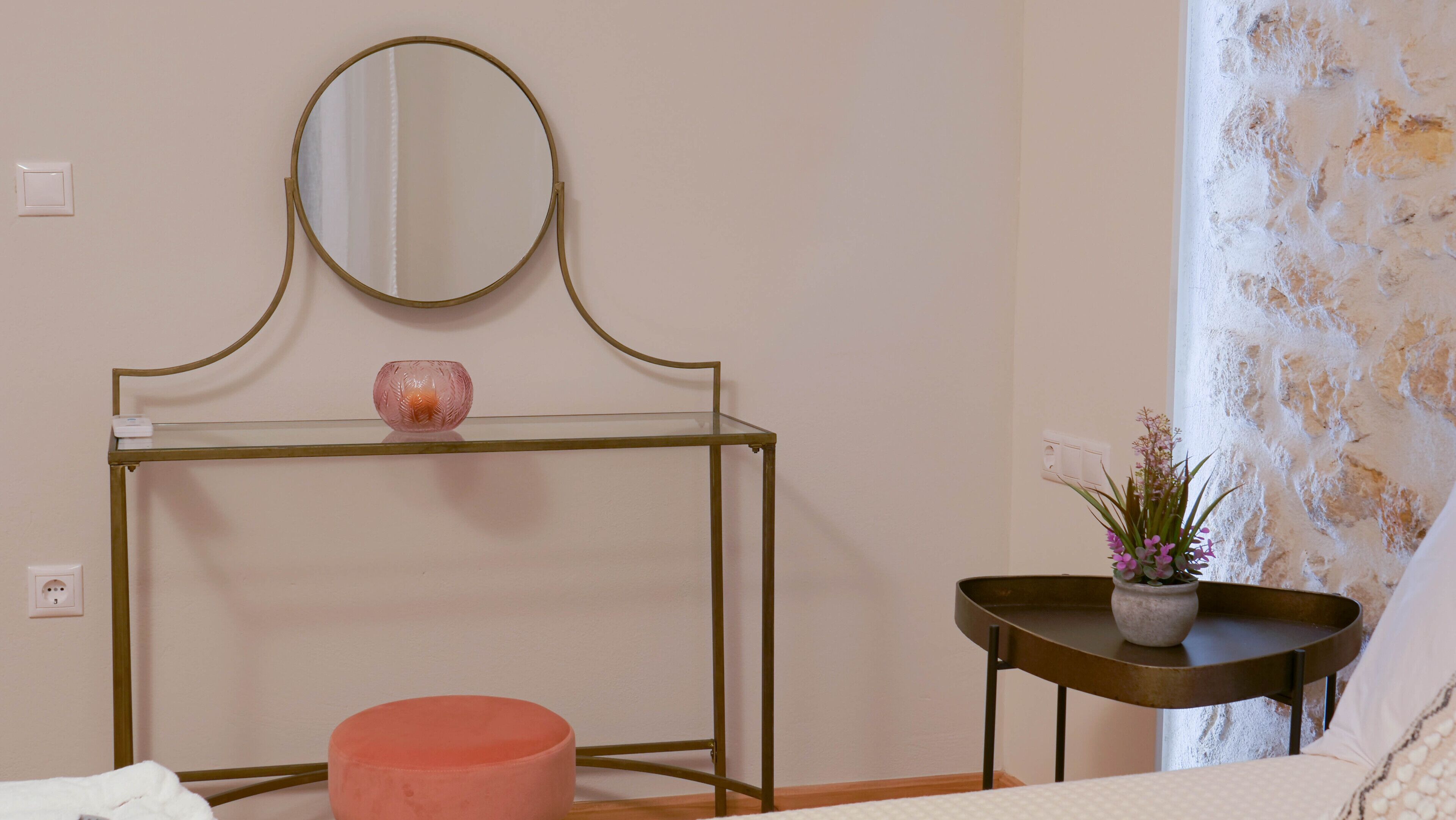 Ein Schlafzimmer mit einem Bett, einem Nachttisch mit einer Vase, einem runden Hocker und einem kleinen Tisch mit einer Pflanze.