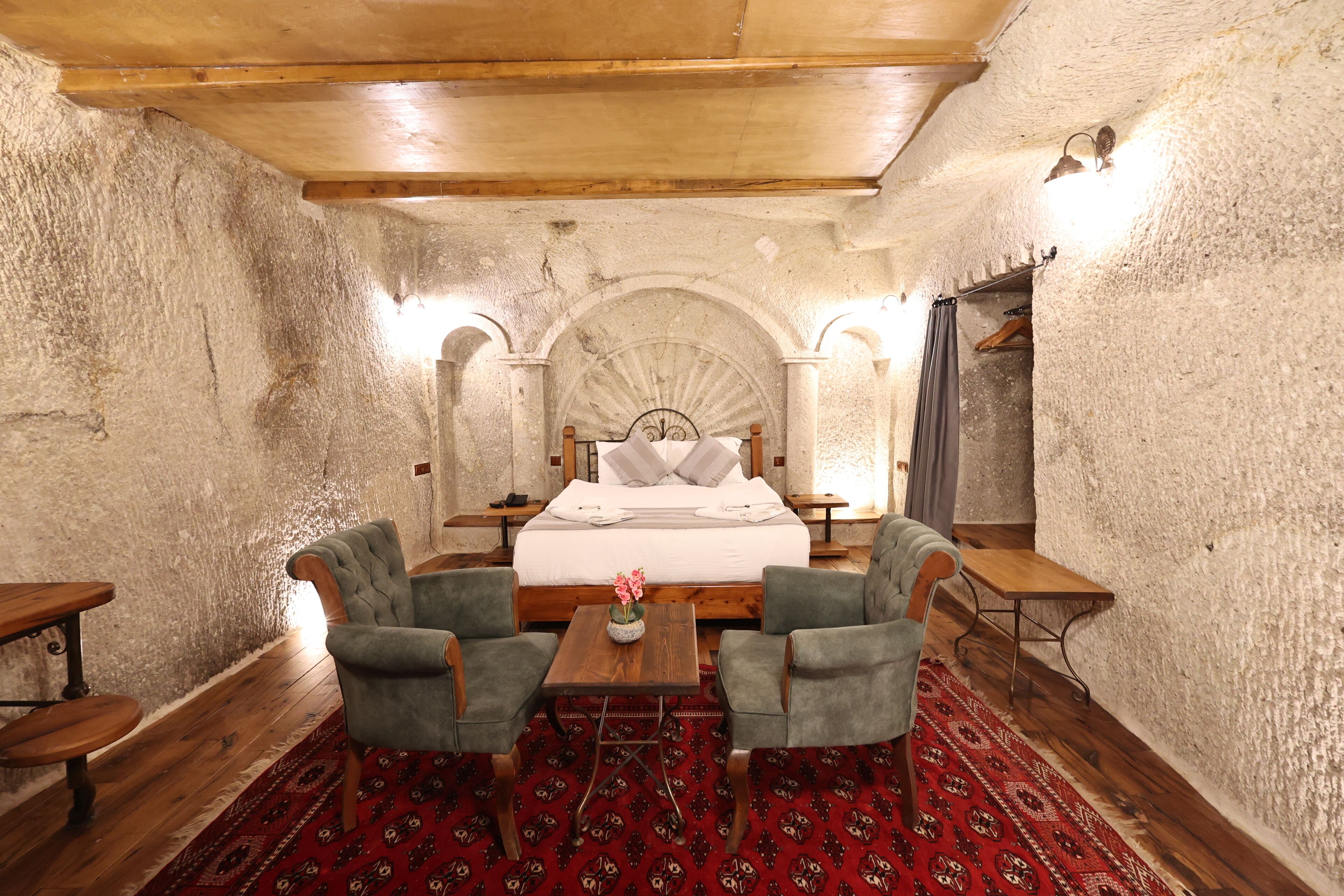 A room with a bed, two armchairs, a small table, and a red patterned rug.