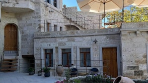 A courtyard with stone buildings, outdoor seating, and a garden area. - Sarnich Cave Suites (Nevsehir)