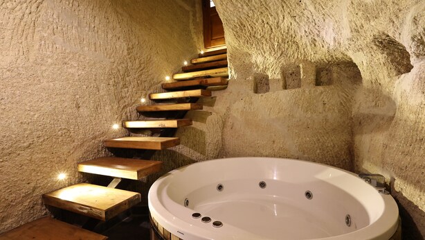 A spa area with a wooden staircase leading to a hot tub against a textured wall. - Sarnich Cave Suites (Nevsehir)