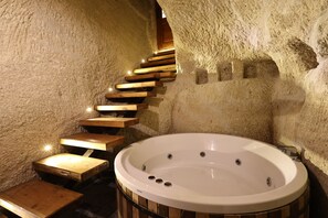 A spa area with a wooden staircase leading to a hot tub against a textured wall. - Sarnich Cave Suites (Nevsehir)