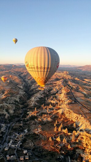 A hot air balloon over a rugged landscape with buildings and roads below. - Sarnich Cave Suites (Nevsehir)