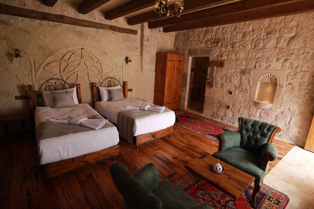 A room with two wooden beds, a green armchair, and a stone wall.