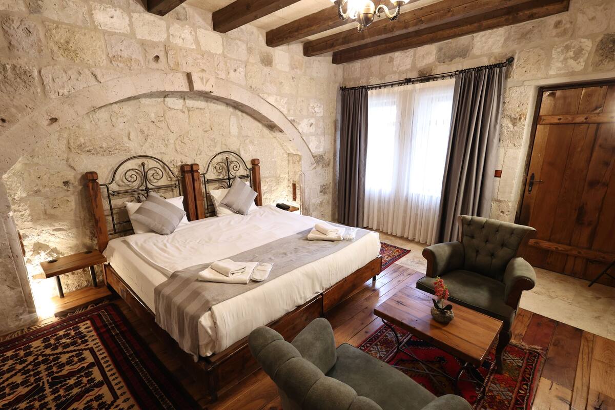 A bedroom with a stone wall, a wooden bed, a chair, and a wooden table.