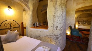 A rustic stone room with a bed, a wooden bench, and a small table with a kettle. - Sarnich Cave Suites (Nevsehir)