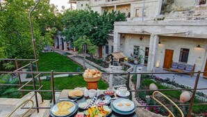 A table set with breakfast items and a view of a courtyard with buildings and greenery. - Sarnich Cave Suites (Nevsehir)