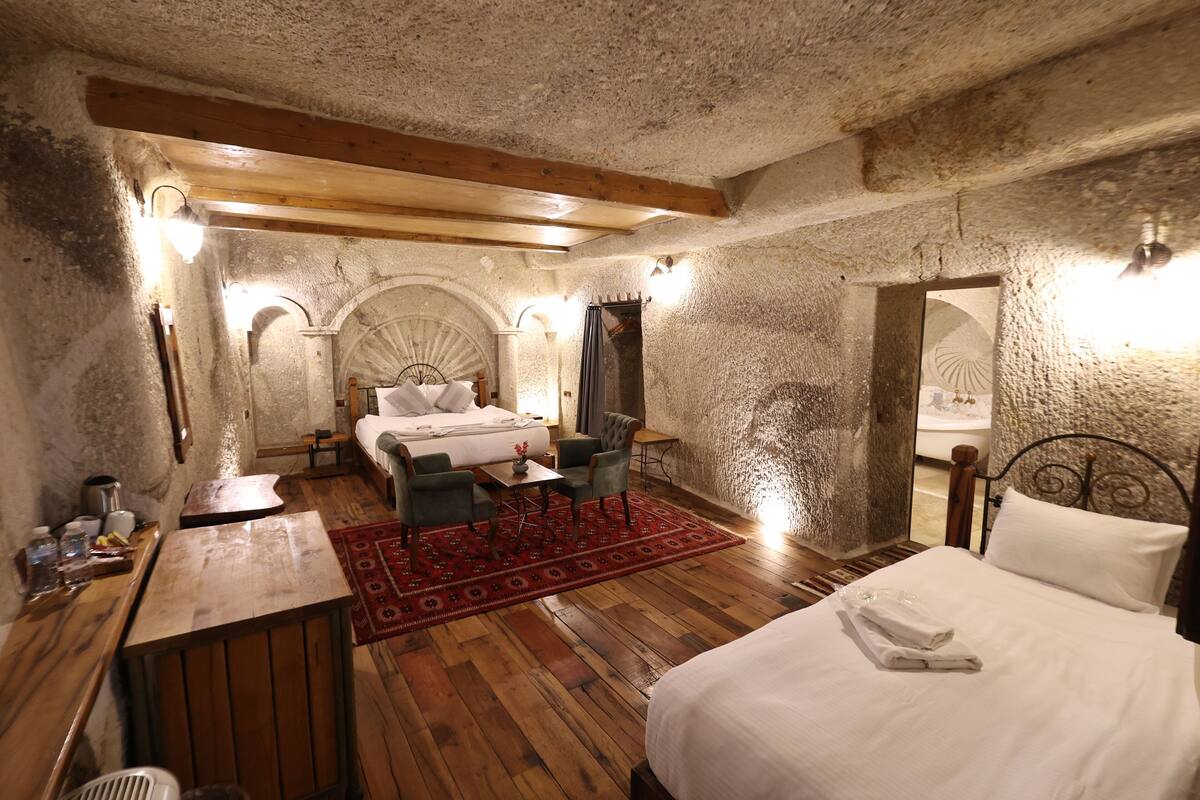 A room with a bed, a desk, and a chair. There are lights on the walls and a wooden ceiling.