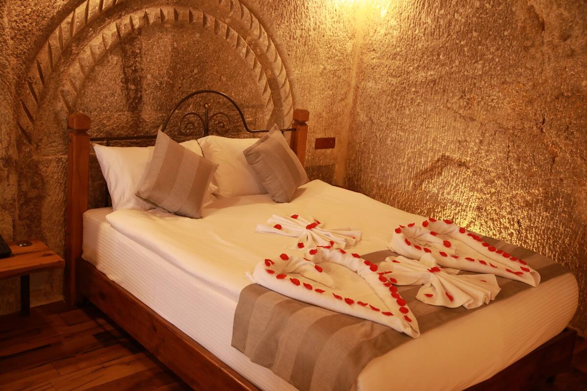 A bed with white linens, a wooden headboard, and a stone wall.