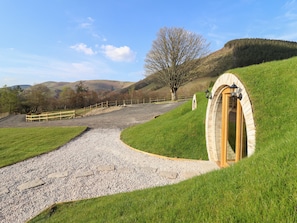 A pathway leading to a stone archway with a lantern on top, surrounded by grassy hills and a clear sky.