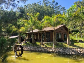 Surrounded by lush greenery, this serene retreat features a traditional structure, a small pond, and a rustic water wheel.