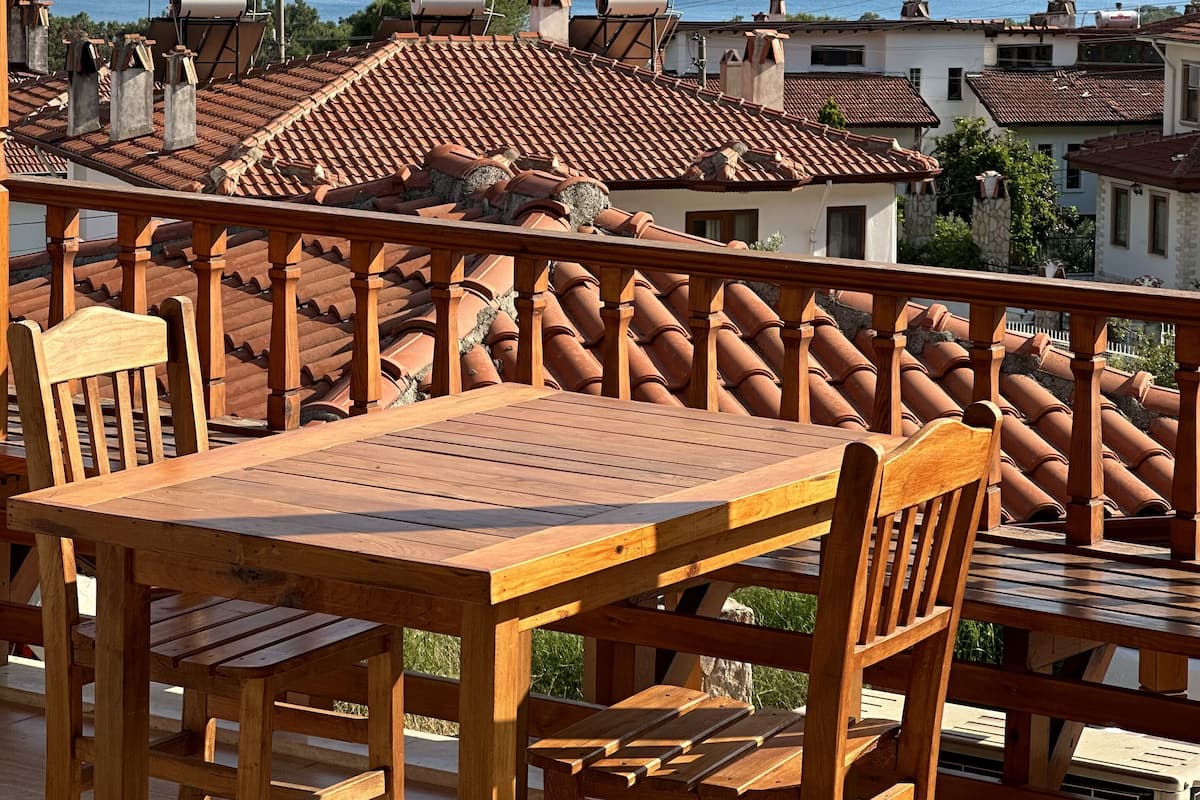 A wooden table and chairs on a balcony overlooking a body of water and hills.