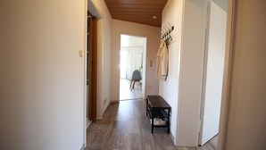 Un pasillo con un banco, suelo de madera y un perchero con ropa colgada.
