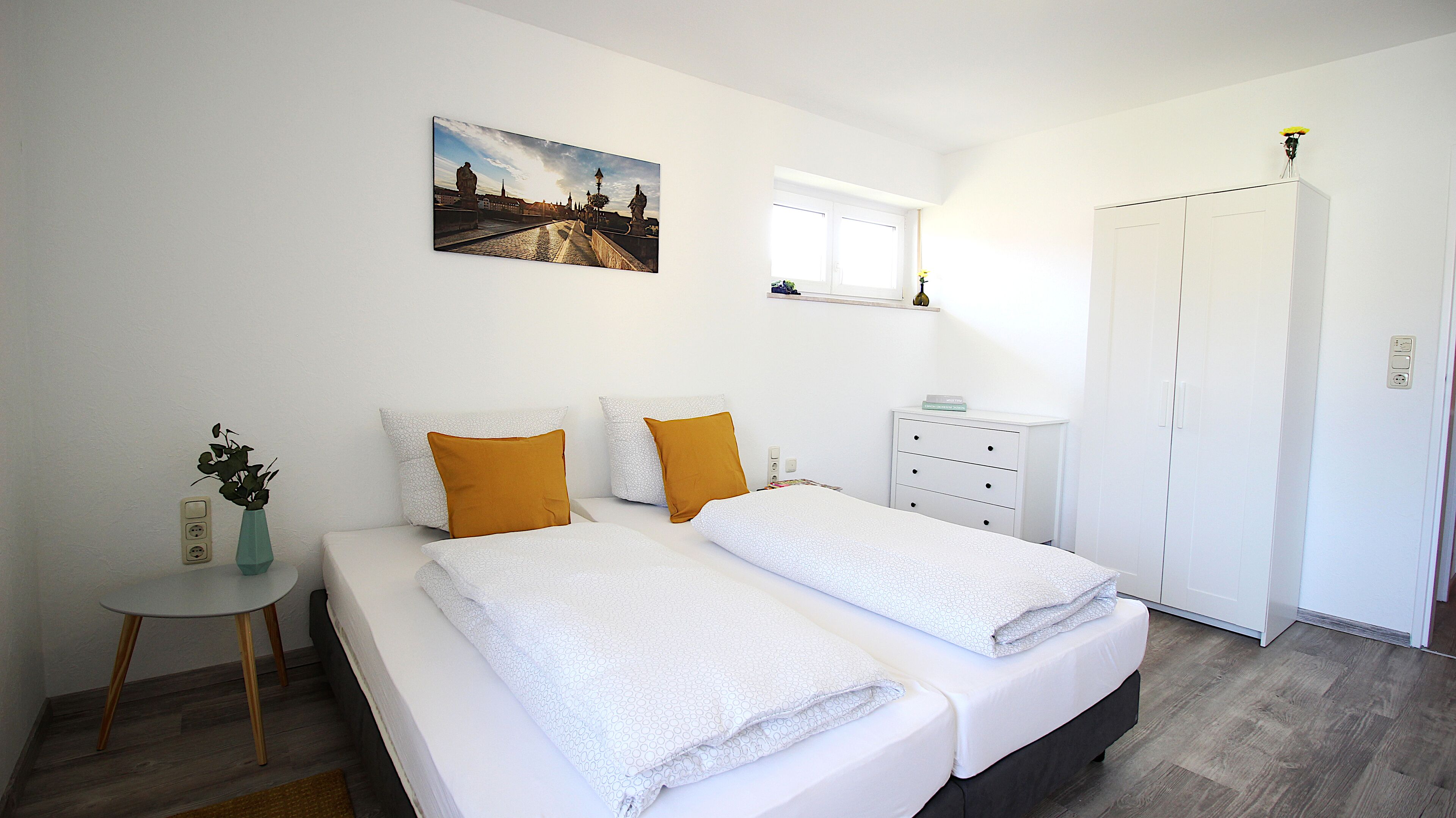 Une chambre avec deux lits, une table de chevet, une commode, une fenêtre et un tableau au mur.