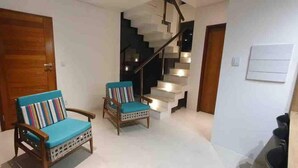 A modern interior with a wooden door, two wooden chairs with blue cushions, a staircase, and a white wall with a light switch. - House with pool on the best beach in Itacimirim! (camaçari)