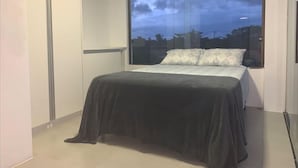 A bedroom with a large window, a bed with a dark cover, and a wall-mounted air conditioner. - House with pool on the best beach in Itacimirim! (camaçari)