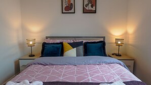 A neatly made bed with a geometric patterned bedspread, two bedside lamps, and a nightstand with a drawer.