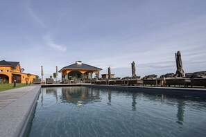 A swimming pool with lounge chairs and umbrellas, surrounded by buildings with a modern design. - Luxus Resort Rügen (Rambin)