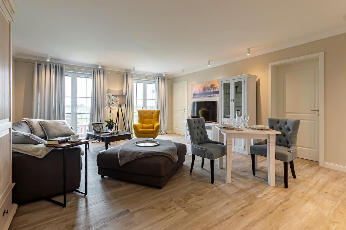 A modern living room with a sofa, ottoman, yellow armchair, grey armchairs, and a dining table.
