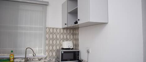 A compact kitchen with a sink, a microwave, and a toaster on the countertop.