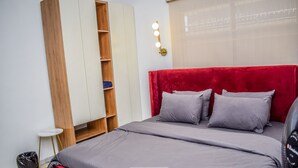 A bedroom with a red headboard, grey bedding, a wooden wardrobe, and a small bedside table. - Stunning 1-bed Apartment in Lekki Phase 1 (Lekki)