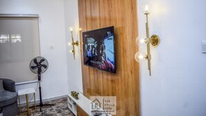 A room with a mounted TV, a standing fan, and wall-mounted lights. - Stunning 1-bed Apartment in Lekki Phase 1 (Lekki)