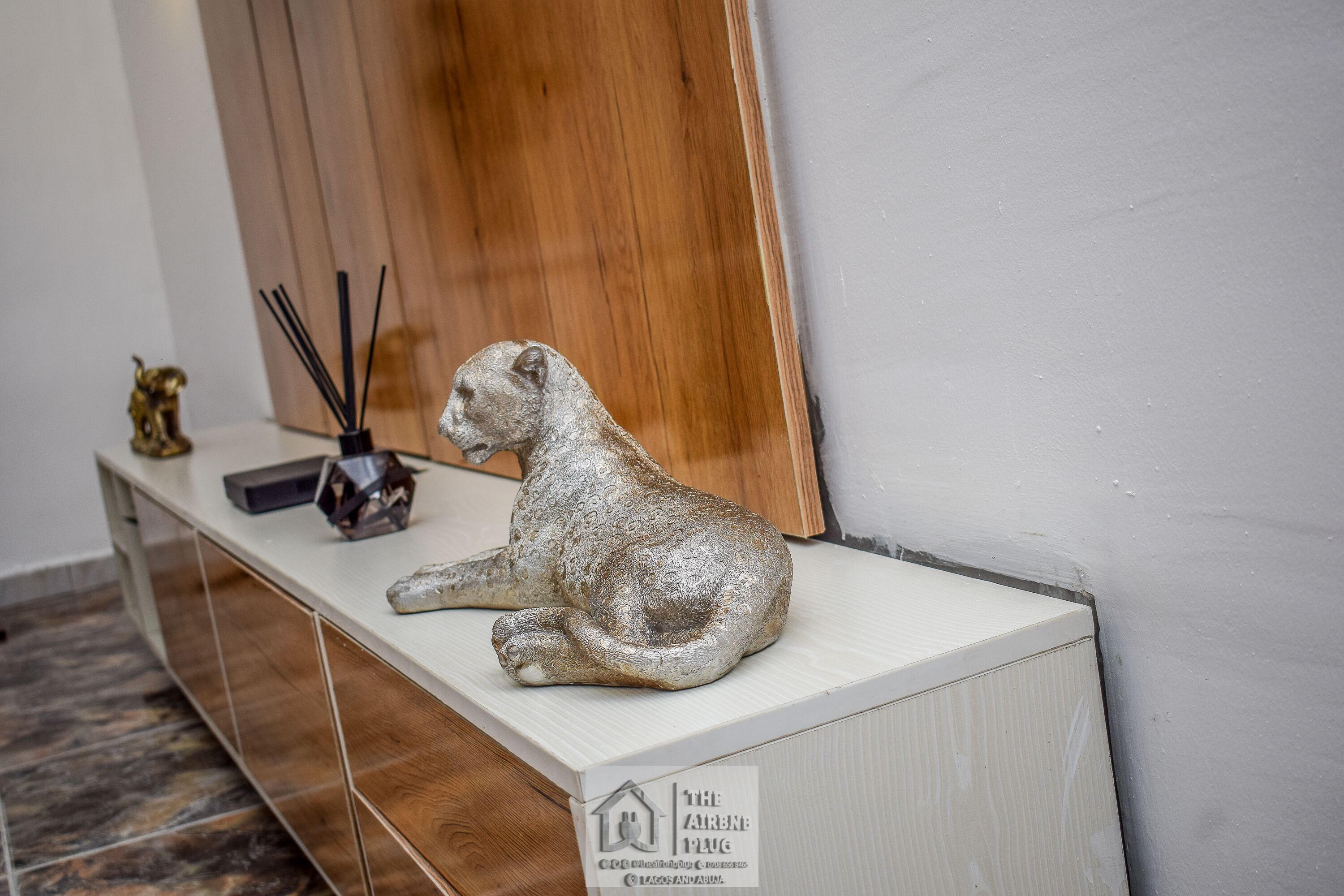 A silver cat statue on a white console table with a wooden panel in the background.