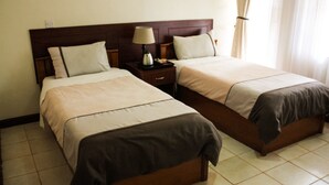 A hotel room with two beds, a nightstand with a lamp, and a window with curtains. - Tawa Country Lodge (Tawa)