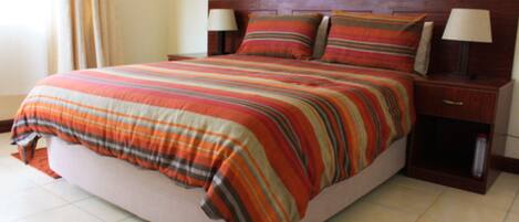 A bed with a striped blanket, two bedside lamps, and a nightstand with a book.