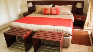 A neatly arranged hotel room with a large bed, two bedside tables with lamps, a red and beige bedspread, and two wooden side tables. - Tawa Country Lodge (Tawa)