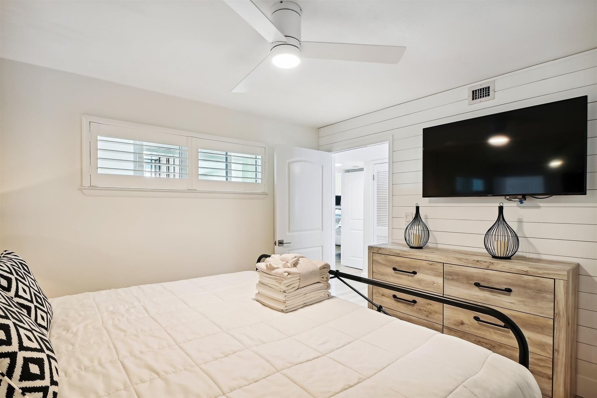 Een slaapkamer met een bed, een dressoir, een televisie en een plafondventilator.
