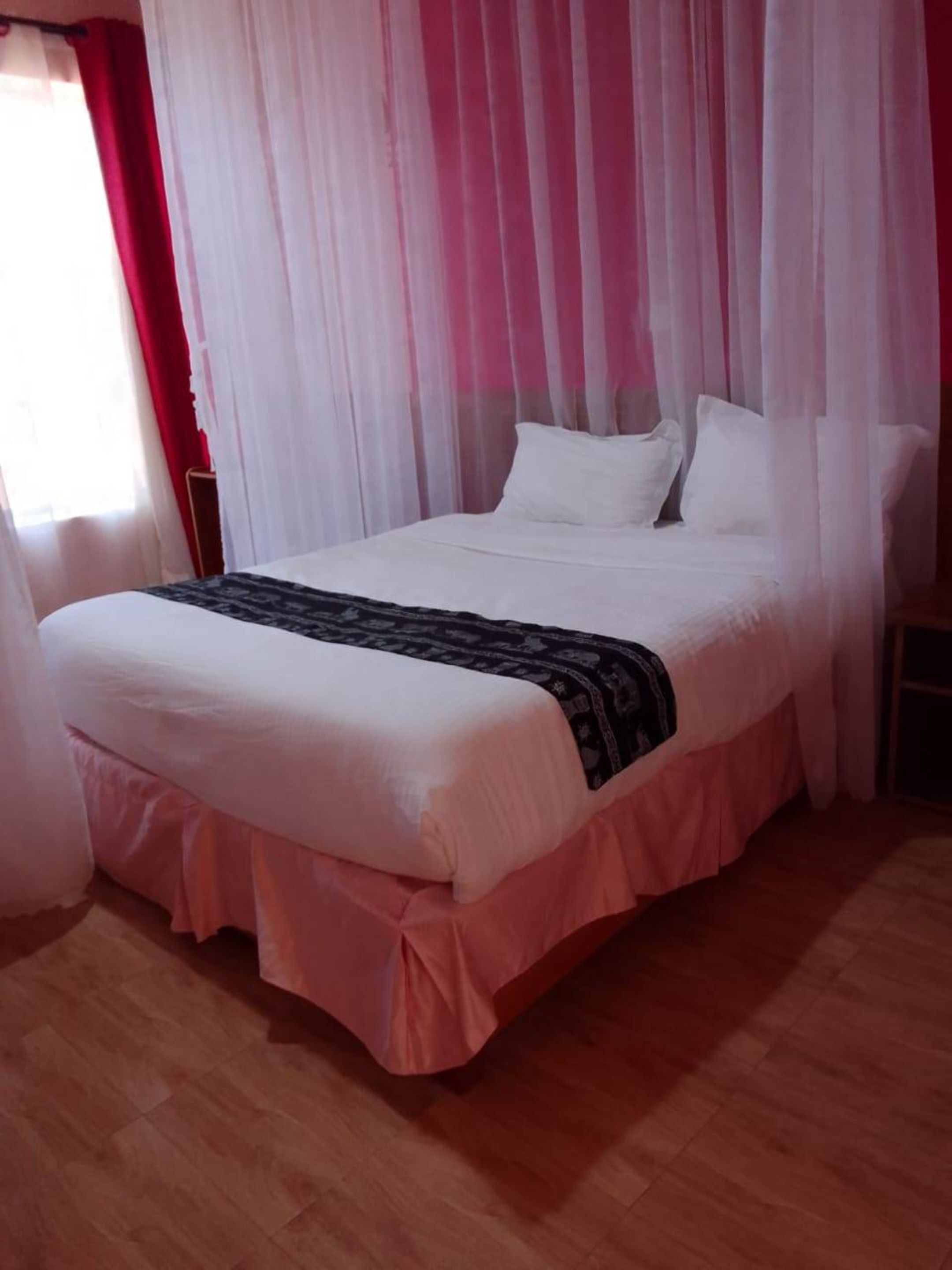 Een slaapkamer met een bed, witte gordijnen en een houten vloer.