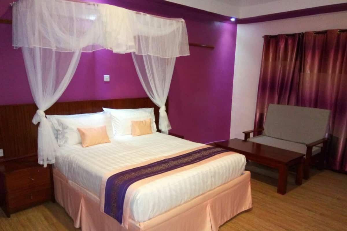 Une chambre avec un grand lit, une table de chevet, une chaise et une fenêtre avec des rideaux.