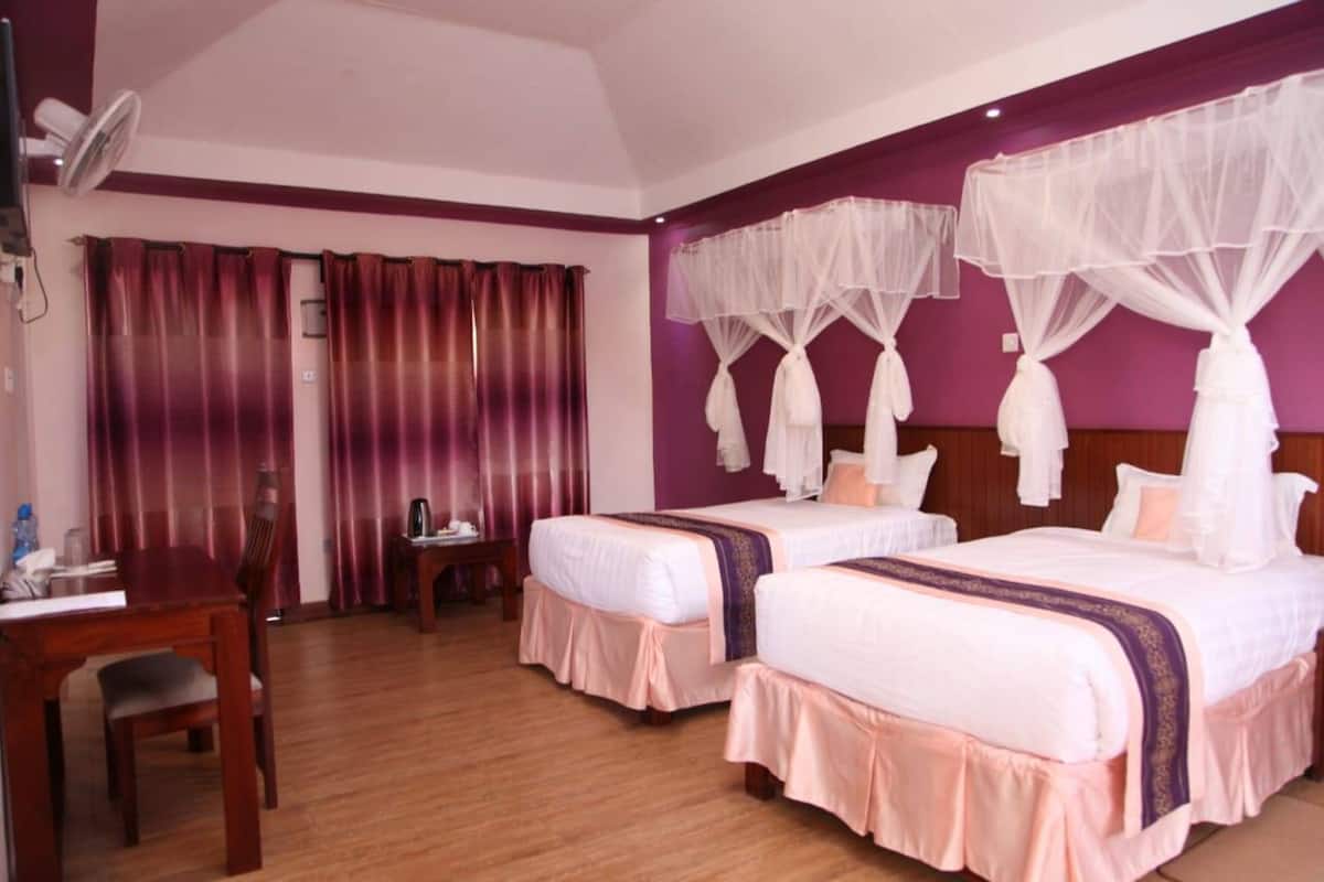 Une chambre d’hôtel avec deux lits, un bureau, une chaise, un ventilateur et une fenêtre avec des rideaux.