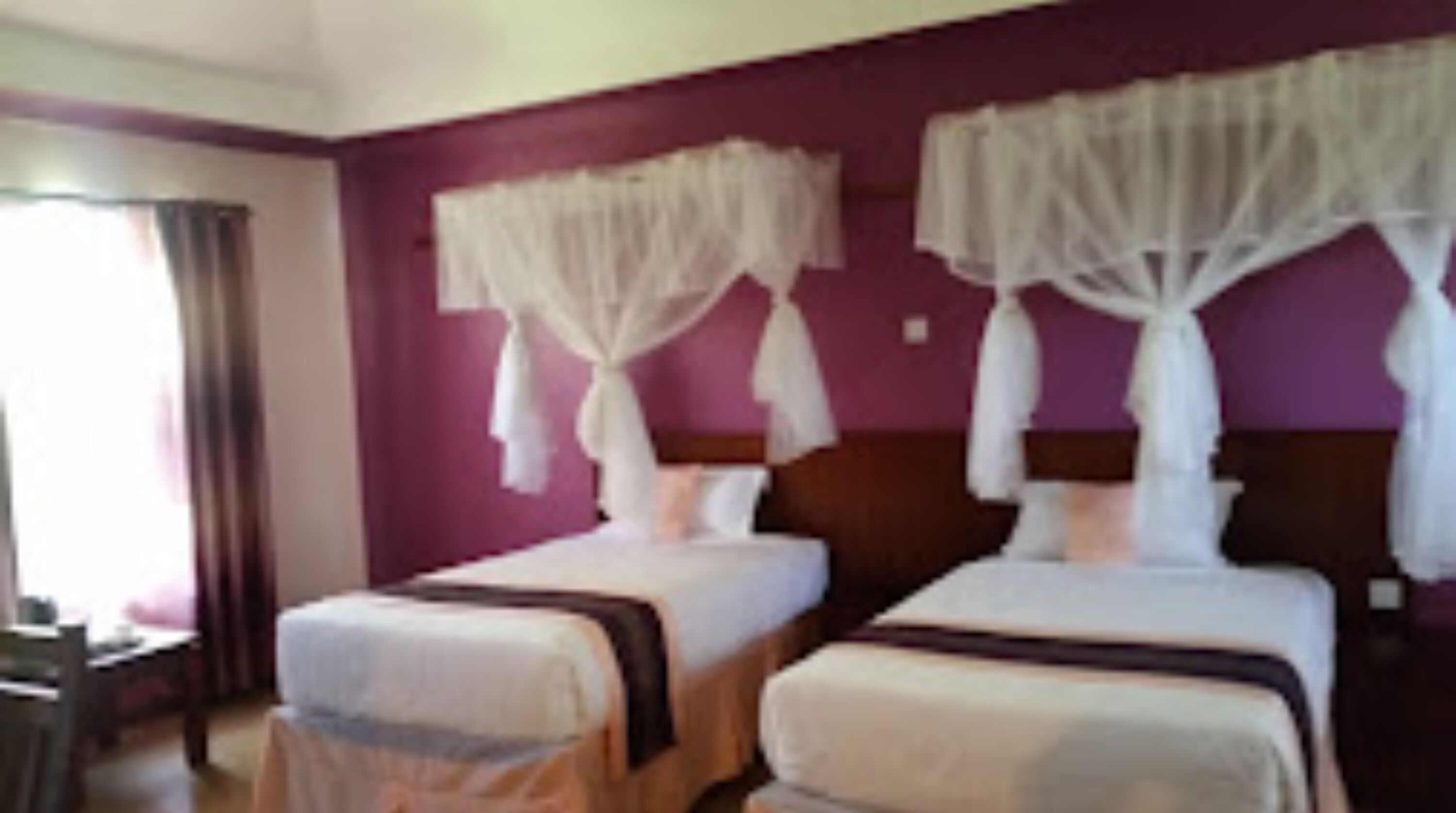Ett hotellrum med två sängar, var och en med ett sänghimmel. Rummet har lila väggar och en sänggavel i trä.