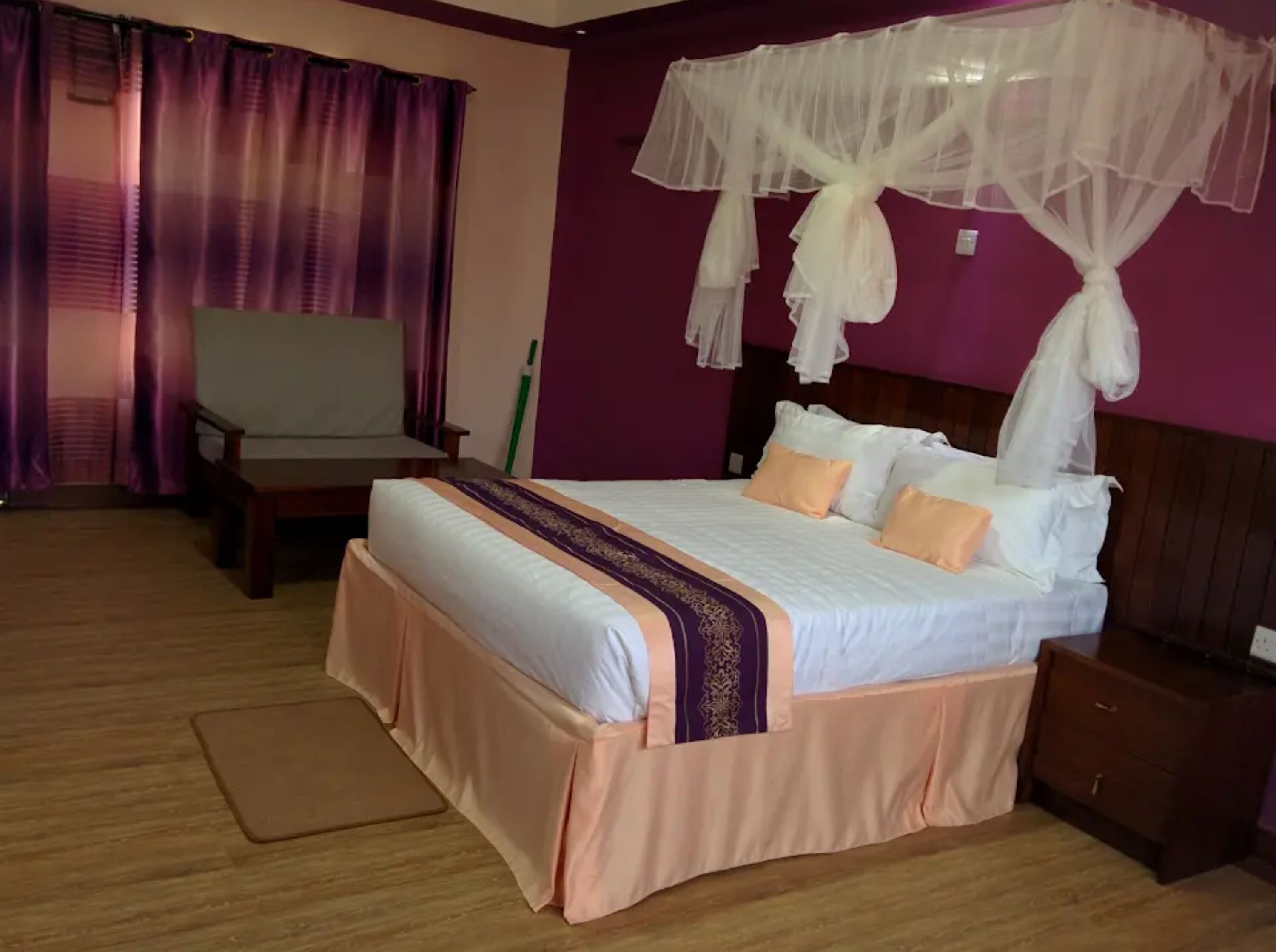 A bedroom with a bed, a nightstand, a chair, and a window with curtains.